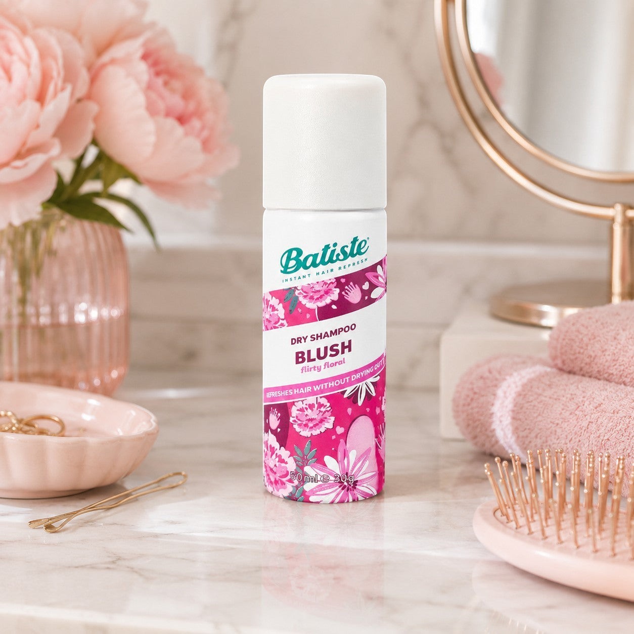 Tap2Own Batiste Blush dry shampoo 50ml travel bottle on a marble vanity with pink flowers and hair accessories.