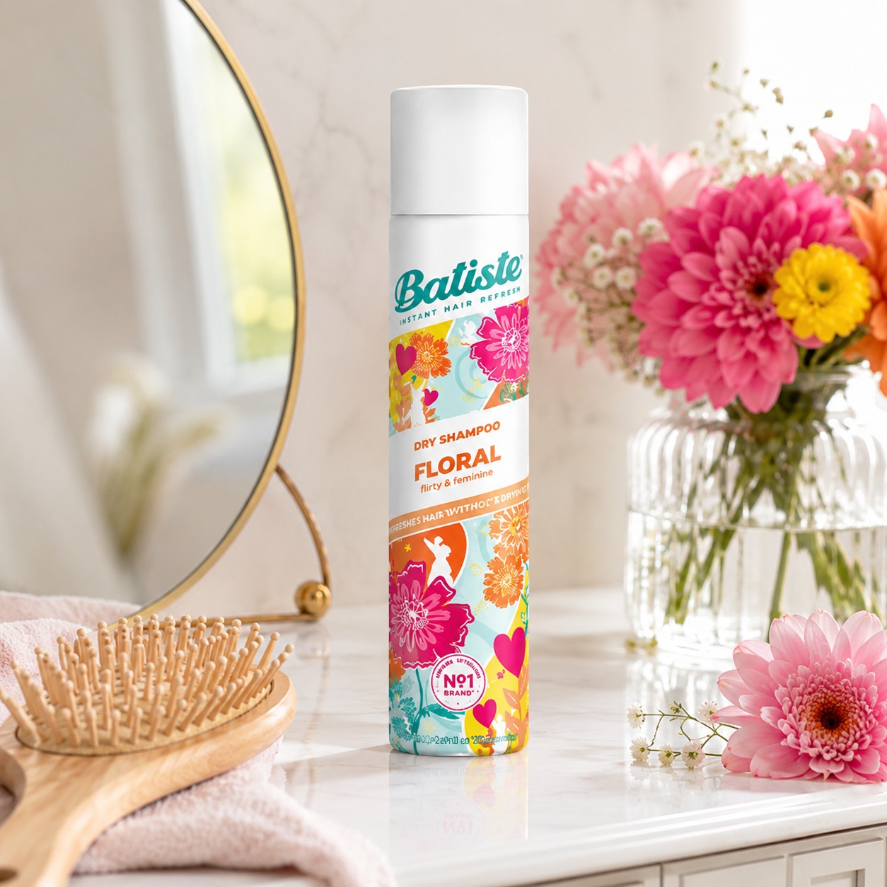 Tap2Own Batiste Floral dry shampoo spray bottle on a marble vanity with a hairbrush and fresh flowers in the background