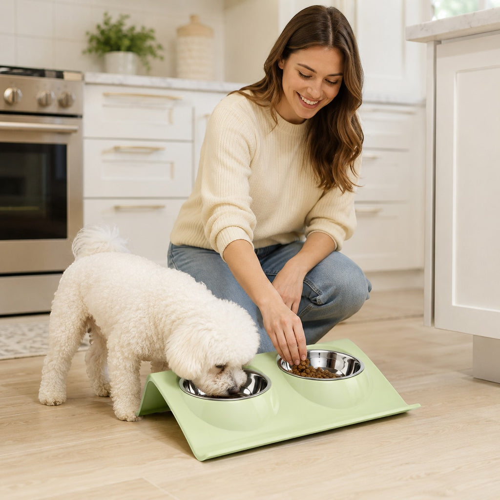 Tap2Own light green elevated double pet bowls with stainless steel inserts, a woman fills one bowl with food.