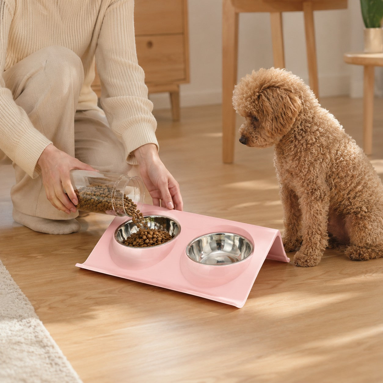 Tap2Own pink elevated double pet bowl feeder with stainless steel bowls, a person fills one bowl with kibble.