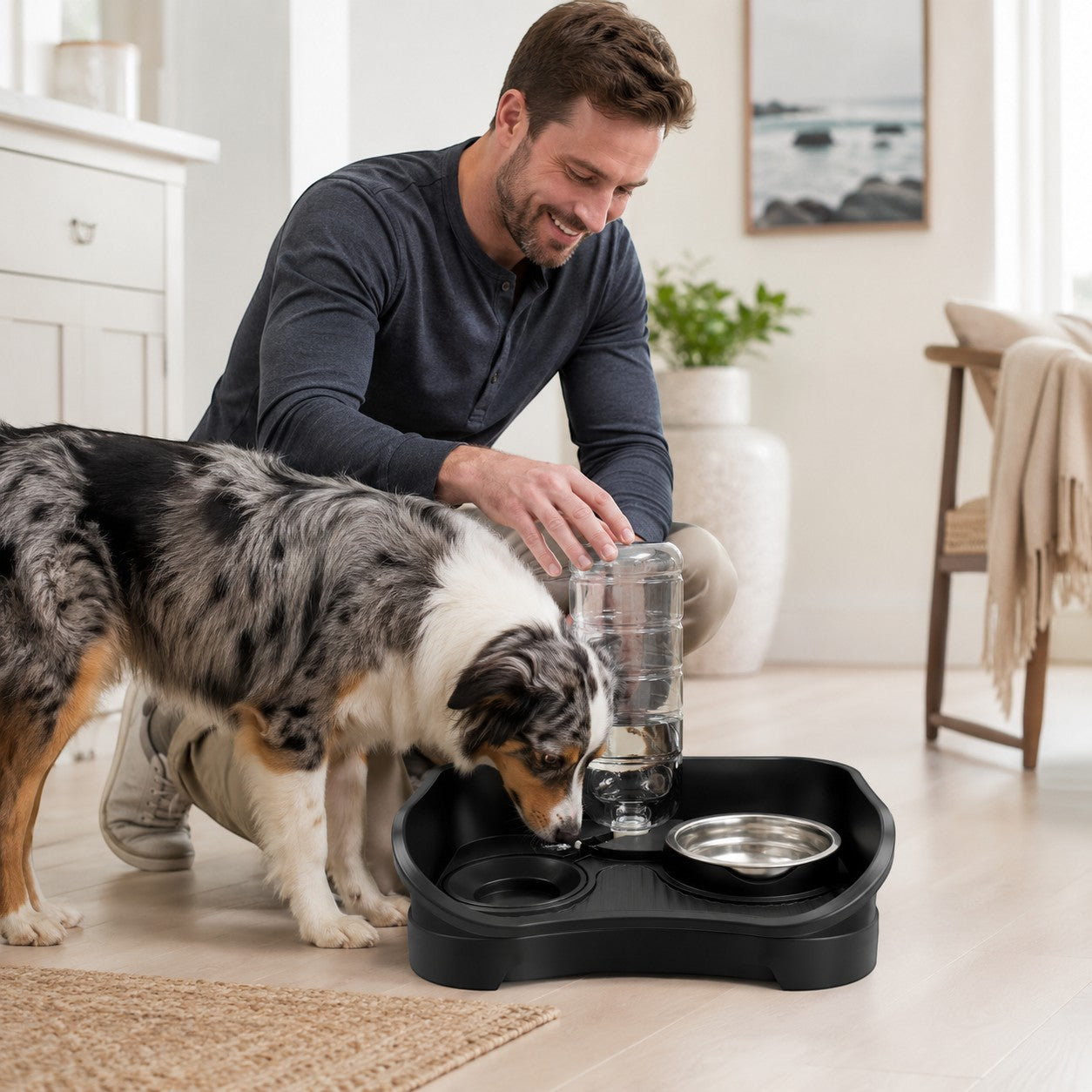 Tap2Own black elevated pet feeding station with automatic water dispenser and stainless steel bowls. A man refills the water bottle for his Australian Shepherd.