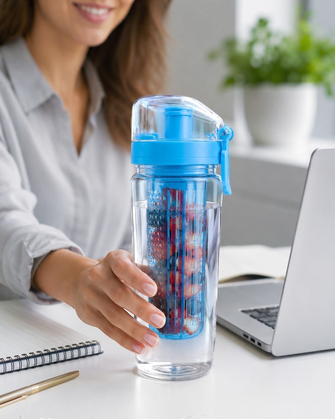 Tap2Own blue and clear BPA-free plastic infuser water bottle with fruit inside, held by a woman at a desk.