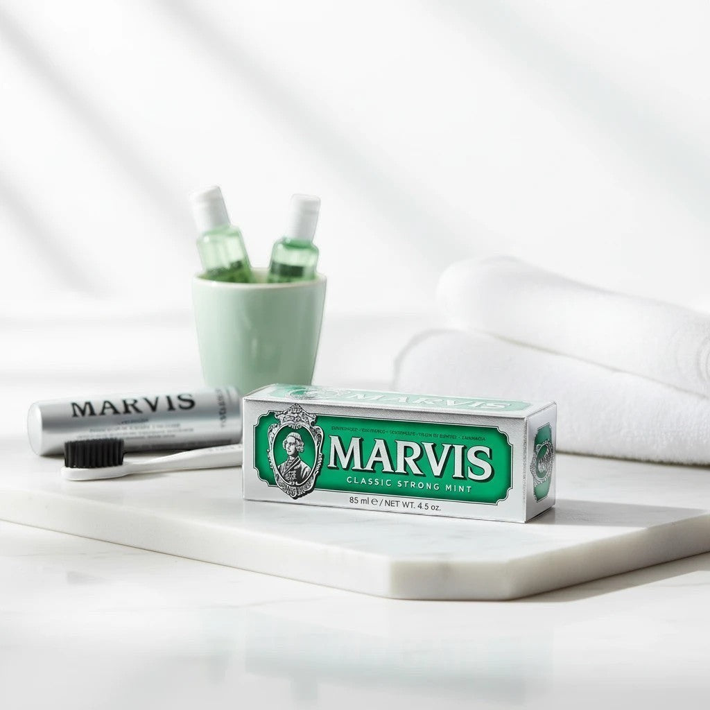 Tap2Own Marvis Classic Strong Mint toothpaste in silver and green packaging on a marble vanity with a toothbrush.