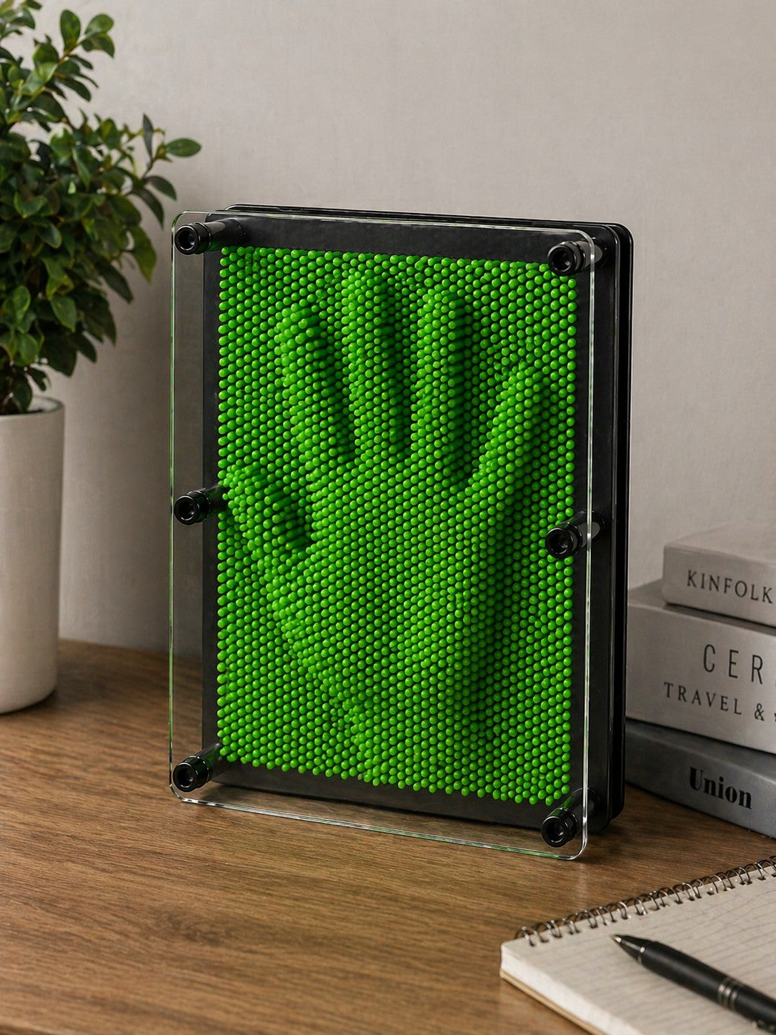 Tap2Own green pin art 3D impression toy creating a hand shape on a wooden desk.