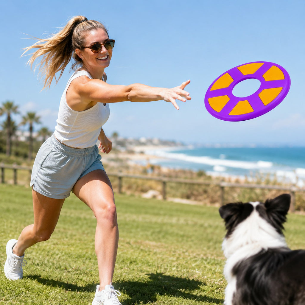 Tap2Own purple and orange rubber flying ring dog toy in mid-air with a woman throwing it and a dog watching.