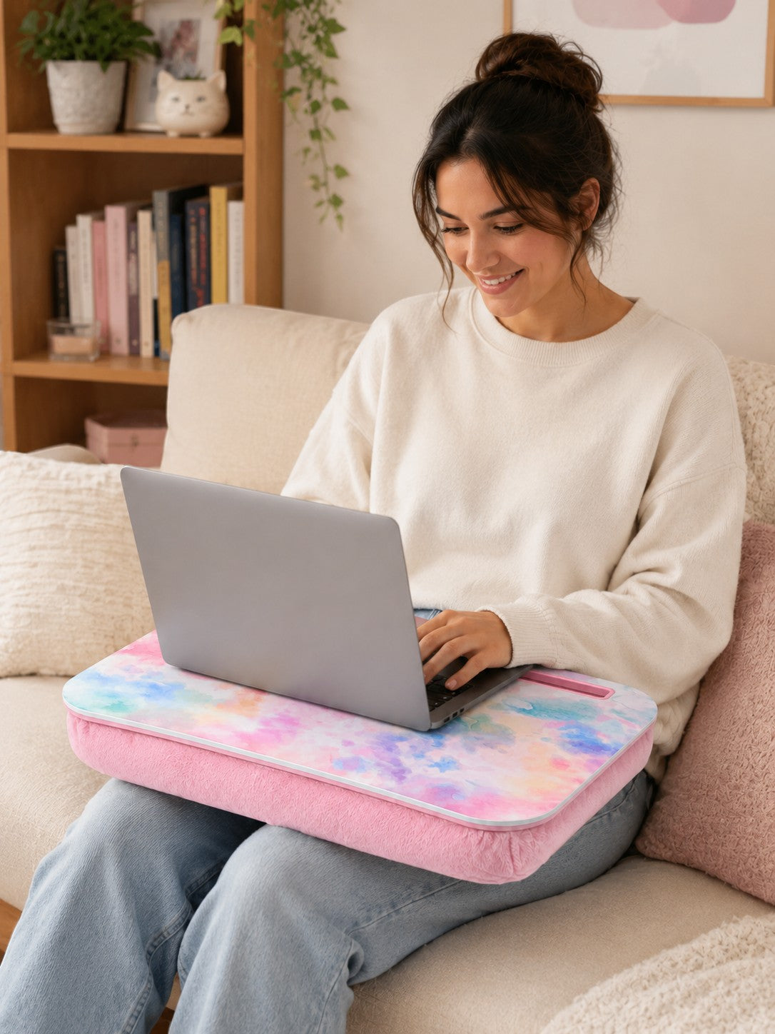 Woman using a Tap2Own tie-dye laptop desk with a pink plush cushion and device slot while sitting on a sofa.