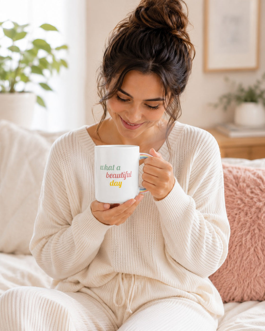 Woman holding a white Tap2Own ceramic mug with a rainbow handle and What a Beautiful Day text in a cozy room.