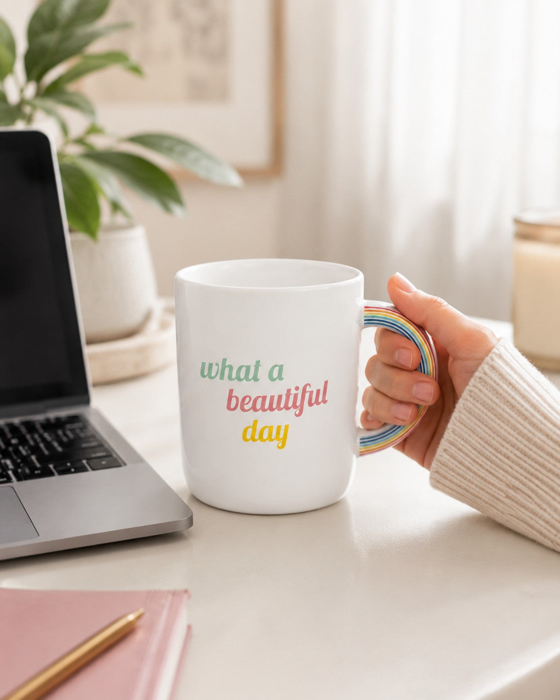 Tap2Own white ceramic mug with rainbow handle and What a Beautiful Day text held on a desk next to a laptop.